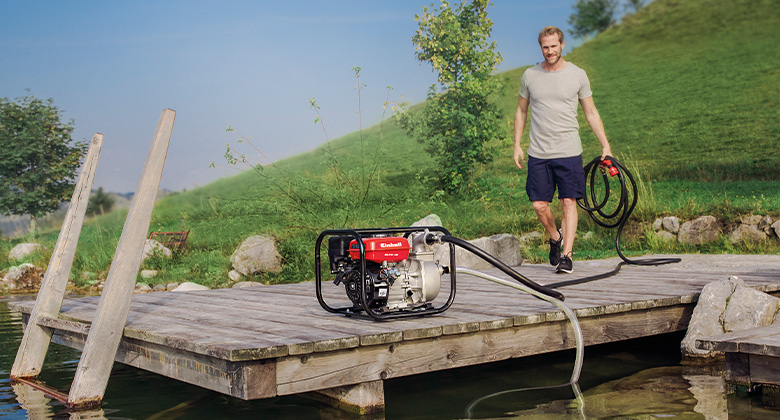 Ein Mann beim Anschließen einer Benzin-Wasserpumpe auf einem Steg über einem Teich.