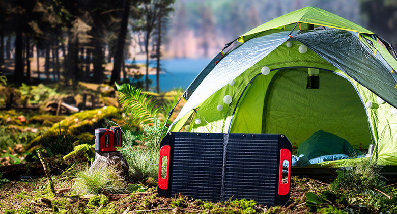 Grünes Campingzelt im Wald mit aufgestelltem Solarpanel und kleinem tragbarem Generator auf dem Boden.
