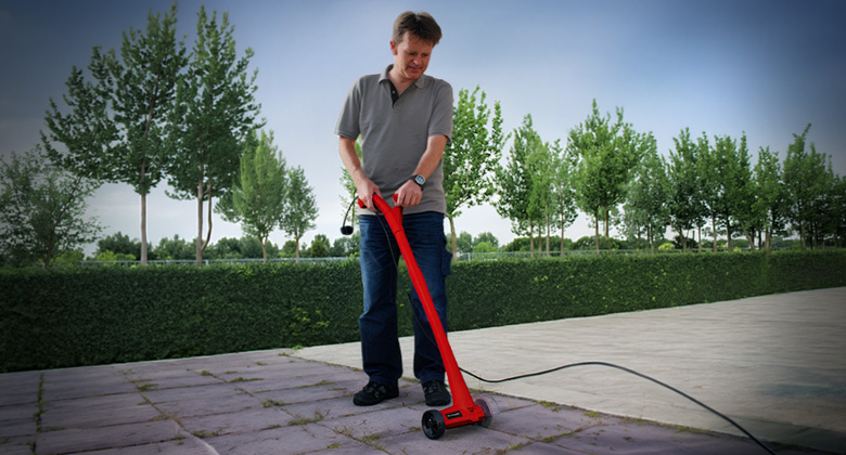 A man cleans paving stones on a patio using a corded electric Einhell patio cleaner.