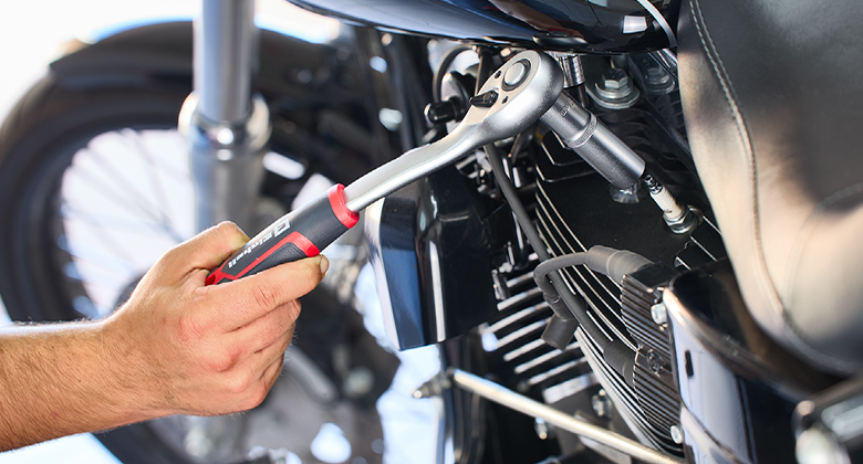 Hand uses an Einhell ratchet wrench to tighten a screw on a motorcycle engine.