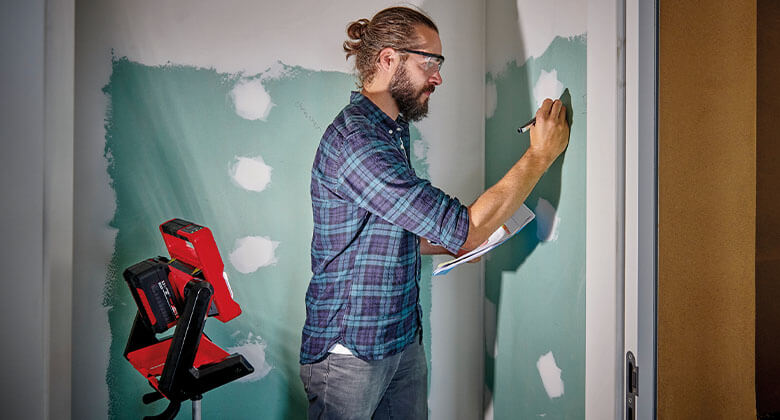 A man works in drywall construction, where he gets light from an Einhell battery-powered construction spotlight.