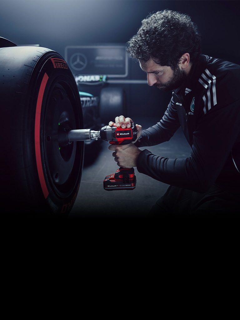 Der Banner zeigt eine Person, die mit einem rot-schwarzen Einhell-Akkuschlagschrauber an dem Rad eines Rennwagens in einer Werkstatt arbeitet.