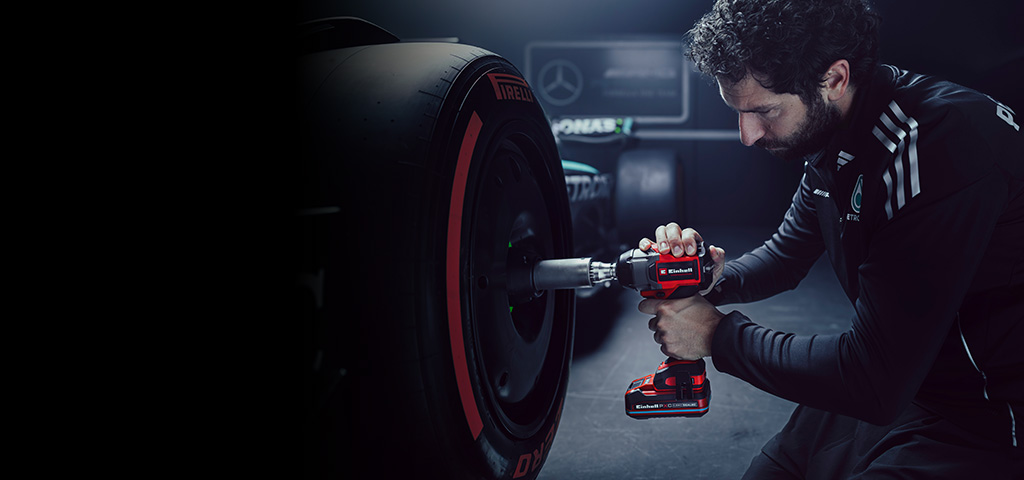 Der Banner zeigt eine Person, die mit einem rot-schwarzen Einhell-Akkuschlagschrauber an dem Rad eines Rennwagens in einer Werkstatt arbeitet.