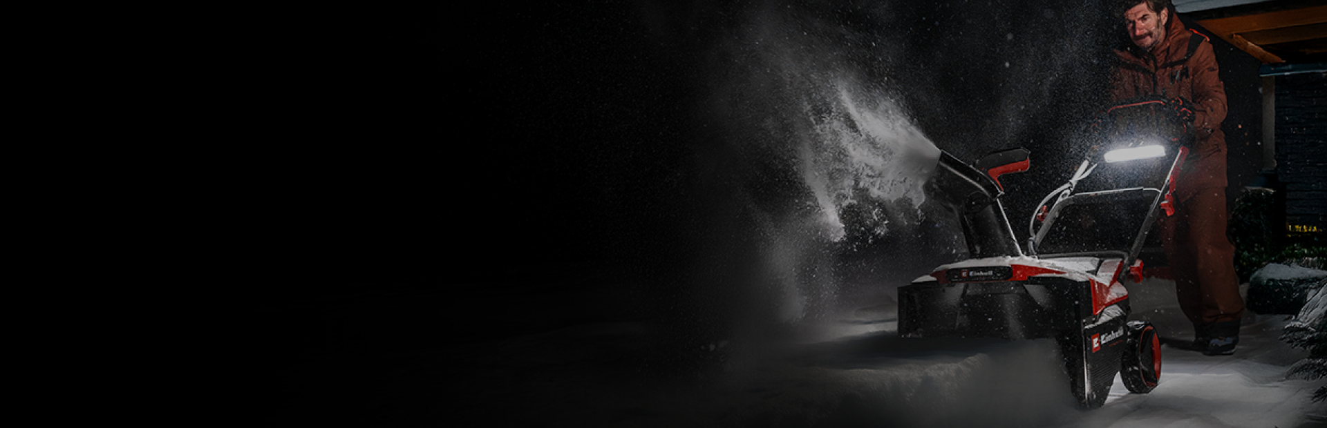 Ein Mann schiebt nachts eine rot-schwarze Schneefräse durch den tiefen Schnee.