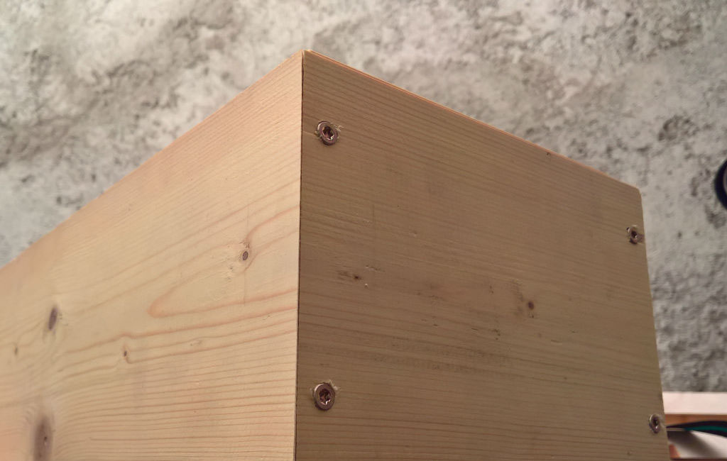Close-up of a corner of a wooden box, fastened with four visible screws.
