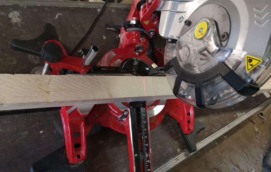 Eine Kappsäge von Einhell schneidet ein Holzbrett, ein roter Laser zeigt die Schnittlinie an.